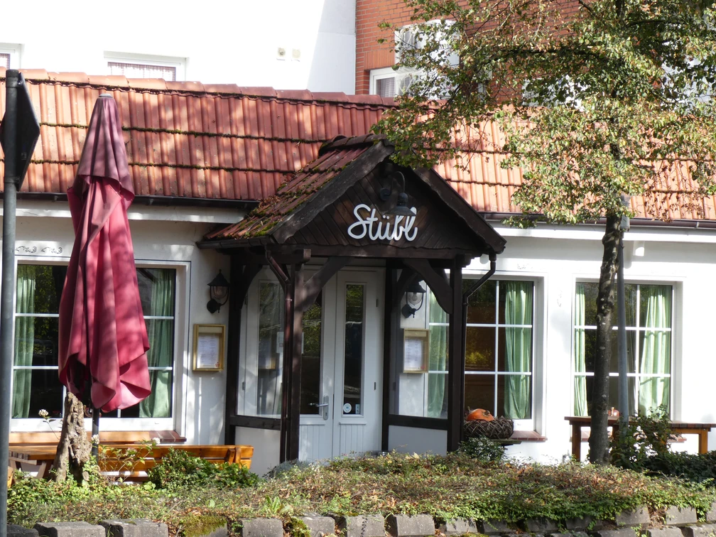Landhaus Wesermarsch Eingang eines traditionellen Gebäudes mit Spitzdach, rotem Ziegeldach und grünen Fensterläden.