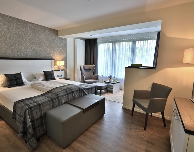 Zimmer Modernes Hotelzimmer mit zwei Einzelbetten, Sitzbereich und großen Fenstern mit Tageslicht.