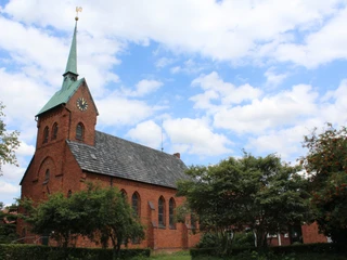 Bartholomäus-Kirche Backsteinkirche Bartholomäus in ländlicher Umgebung, grüner Kirchturm, blauer Himmel mit Wolken.