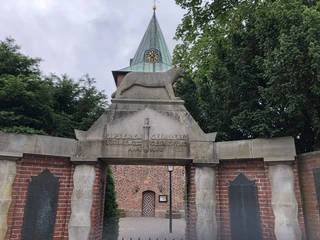 Denkmal f. d. Gefallenen und Vermissten des 1.u.2. Weltkrieges Denkmal aus Stein mit Löwenfigur und Inschrift für Gefallene beider Weltkriege, Kirche im Hintergrund.