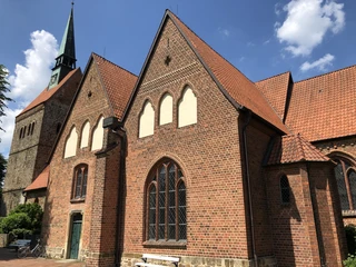Backstein-Gotik Kirche mit hohem Turm und spitzen Fenstern; blauer Himmel mit wenigen weißen Wolken.