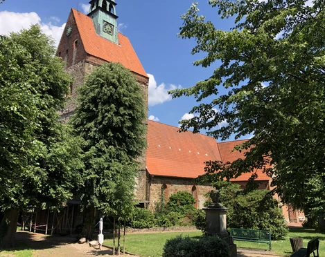 Kirche Vilsen Eine historische Kirche mit rotem Ziegeldach und Turm, umgeben von Bäumen, unter blauem Himmel.