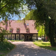 Ein Fachwerkhotel im Grünen, umgeben von Bäumen, mit gepflastertem Weg zum Eingang.