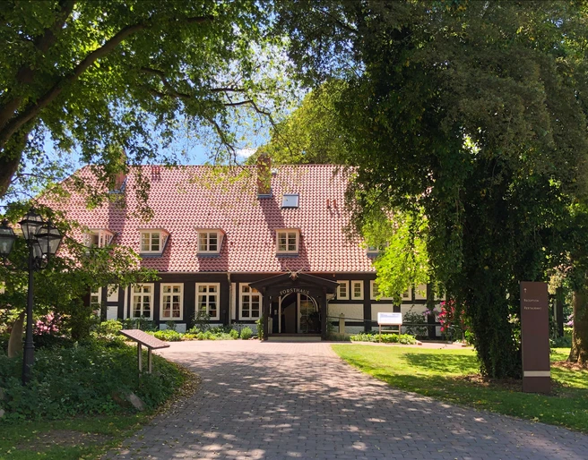 Hotel Forsthaus Heiligenberg Ein Fachwerkhotel im Grünen, umgeben von Bäumen, mit gepflastertem Weg zum Eingang.