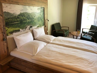 Ein modern eingerichtetes Hotelzimmer mit Holzdetails, einem Doppelbett, kleinen Tisch und zwei Sesseln.