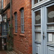 Historische Backsteinfassade eines Hotels mit blauen Fenstern und Türen in einer schmalen Gasse.