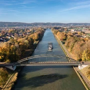 Panoramablick auf den Mittellandkanal bei Bad Essen Brücke über einen herbstlichen Fluss mit Frachtschiff, umgeben von buntem Laub.