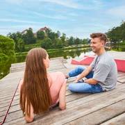Relaxen am Charlottensee in Bad Iburg Ein Mann und eine Frau sitzen entspannt auf einem Holzsteg am See, im Hintergrund grüne Bäume.