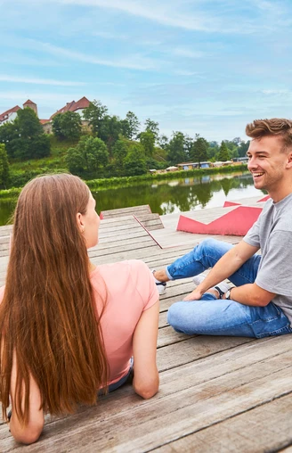 Relaxen am Charlottensee in Bad Iburg Ein Mann und eine Frau sitzen entspannt auf einem Holzsteg am See, im Hintergrund grüne Bäume.