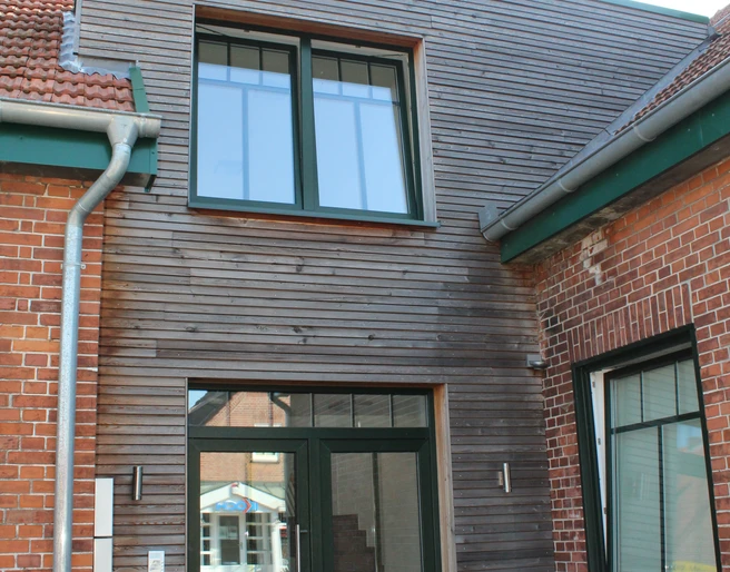 Gästezimmer Bär Backsteinbau mit modernem Holzanbau, zwei großen Fenstern und Türen, im Innenhof mit Pflanzen.