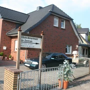 Zweistöckiges Backsteinhaus mit Parkplatz und einem Schild "Gäste Appartement im Zentrum" im Vorgarten.