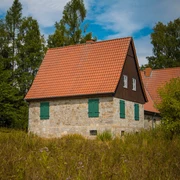 Aahäuser bei Bleiwäsche Ein Steinhaus mit rotem Ziegeldach und grünen Fensterläden, umgeben von Bäumen unter blauem Himmel.