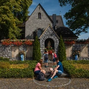 Zwei Erwachsene und drei Kinder sitzen vor einer Steinmauer einer Kirche mit roten Blumen geschmückt.