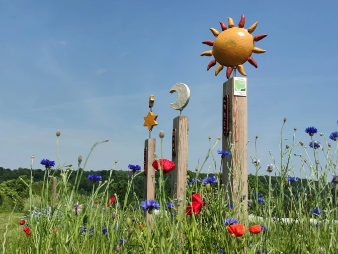 Skulpturen an Tor zum Sauerland Verschiedene bunte Skulpturen ragen aus einem Feld mit blühenden Mohn- und Kornblumen empor.