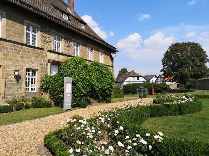 Historisches Schloss Gehrden mit gepflegten Hecken und blühenden Rosen im sonnigen Garten.
