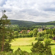Blick auf Schloss Willebadessen inmitten grüner Landschaft, umgeben von bewaldeten Hügeln und Feldern.
