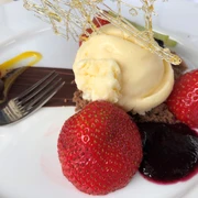 Eis Dessert Vanilleeis auf Schokoladenboden, umgeben von frischen Erdbeeren und Beerenpüree, garniert mit filigranem Karamell.