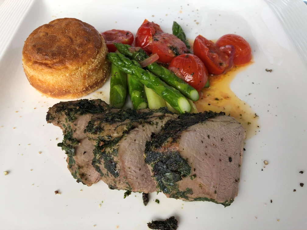 Schweinefilet mit feiner Kräuterkruste, begleitet von Spargel, Tomaten und einem kleinen Soufflé.