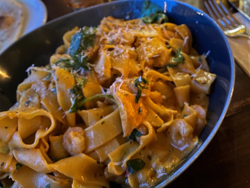 Nudeln Hausgemachte Bandnudeln mit cremiger Sauce, frischen Kräutern und Käsespänen in blauer Schale.