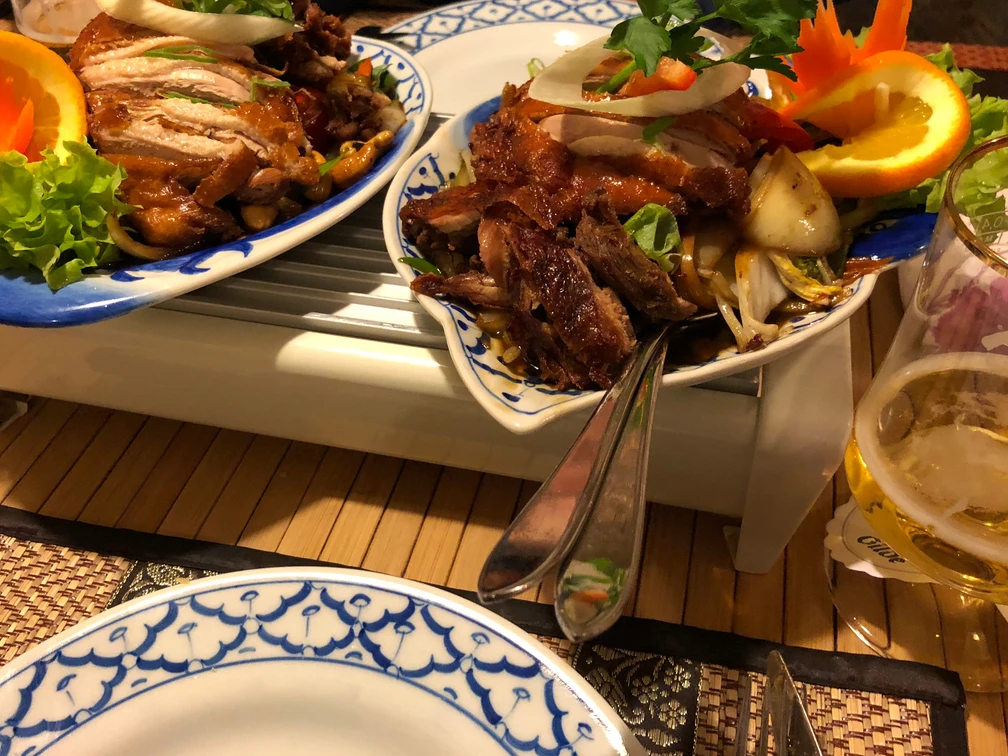 Chinesisches Gericht Knusprig gebratenes Entengericht auf Porzellanteller mit frischen Orangenscheiben und Gemüsebeilage.