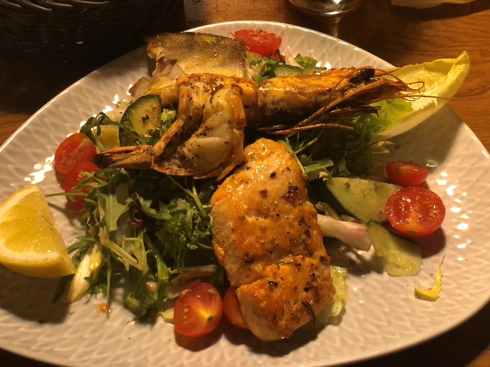 Salat und Fisch Ein Teller mit gebratenem Fisch, Riesengarnele und frischem Gemüsesalat aus Tomaten und Gurken.