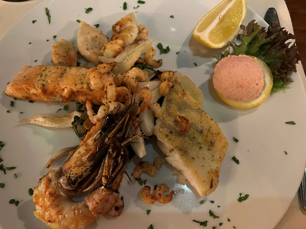 Fischteller Ein Teller mit verschiedenen Fischsorten, Garnelen und einer Zitronenspalte auf dekorativem Salat.