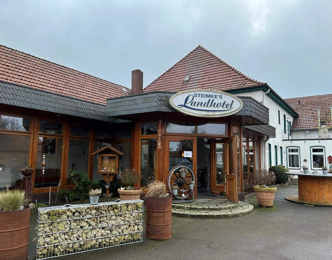 Steimkes Landhotel Eingang Eingang von Steimkes Landhotel mit runden Fenstern, Schindeldach und dezent begrünten Pflanzkübeln.