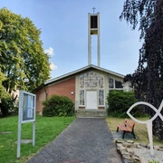 Evangelische Kirche mit hohem Glockenturm, gelegen in einer grünen Umgebung mit Parkbank und Gehweg.