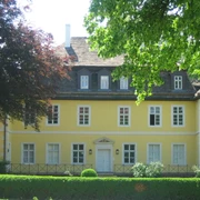 Bökerhof  Historisches gelbes Herrenhaus mit weißen Fensterrahmen, umgeben von üppigem Grün und Bäumen.