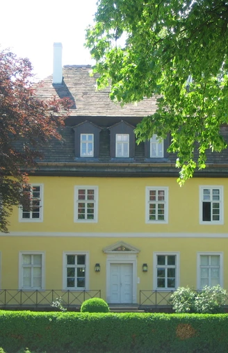 Bökerhof  Historisches gelbes Herrenhaus mit weißen Fensterrahmen, umgeben von üppigem Grün und Bäumen.
