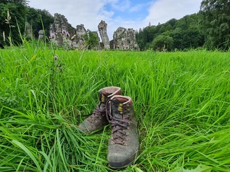 Wandern an den Externsteinen Wanderschuhe im Vordergrund einer grünen Wiese mit den imposanten Felsen der Externsteine.