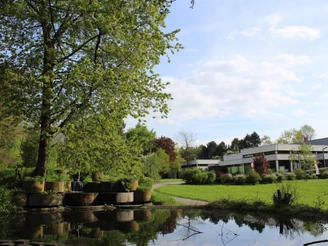 Das Bad Meinberger Badehaus umgeben von Grünflächen, Bäumen und einem Teich bei sonnigem Wetter.