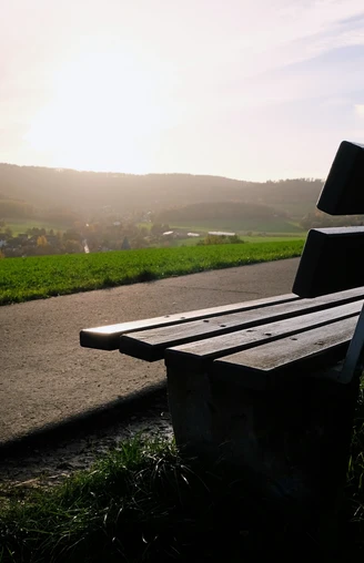 Aussichtspunkt Eine Holzbank steht am Wegesrand mit Blick über ein Dorf, beleuchtet von der Abendsonne.