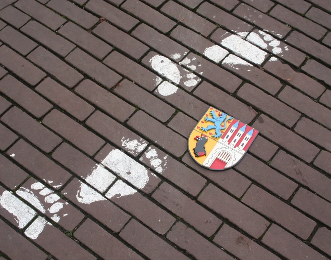 Nienburger Bärenspur Spur von Bärentatzen und Stadtwappen auf gepflastertem Weg in Nienburg, Anregung zum Stadtrundgang.