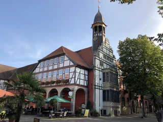 Rathaus Nienburg Rathaus Nienburg mit Fachwerk und Uhrturm, umgeben von Bäumen und einem Café im Vordergrund.