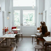 Innenansicht Café Analog - Cafés in Leipzig Zusehen sind die Sitzplätze des Cafés: Kleine Tische und Bänke aus Holz sowie kleine Bilder, die an der Wand hängen. Der Raum wird von einem großen Glasfenster erhellt, Cafe, Gastronomie, Freizeit