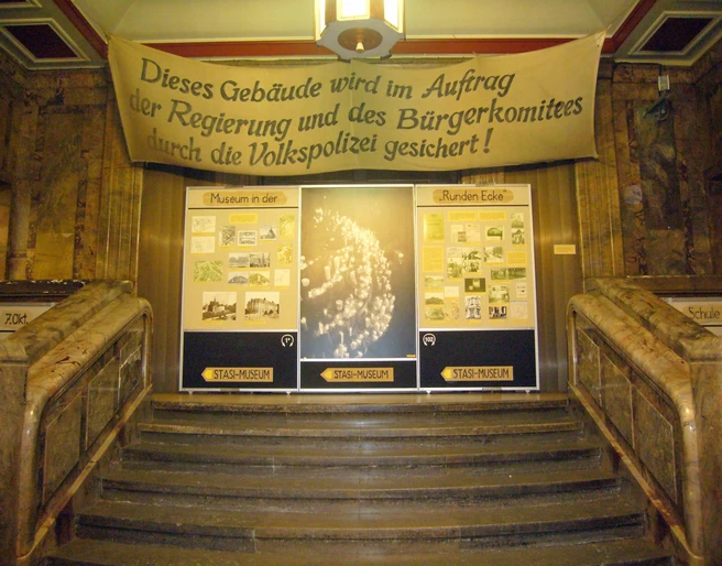 Treppenaufgang im Museum in der Runden Ecke - Friedliche Revolution in Leipzig Blick vom unteren Ende des Treppenaufgangs auf mehrere Banner und Poster, die auf das Museum in der Runden Ecke hindeuten, Friedliche Revolution, Geschichte, Freizeit, Sehenswürdigkeiten