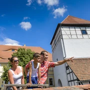 Burg Düben - Leipzig und Region mit Kindern Eine Familie mit Kind steht auf dem Gelände der Burg Düben im Sonnenschein und schaut sich die Umgebung an, Familie, Ausflug, Freizeit, Kultur