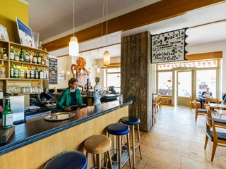 Café Cantona - Gastronomie Leipzig Gastraum des Café Cantona mit langer Bar und Barstühlen sowie einer großen Fensterfront mit Blick auf die Windmühlenstraße