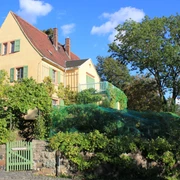 Göschenhaus Grimma mit Göschengarten Das Göschenhaus in Grimma, ein malerisches, gelb gestrichenes Fachwerkhaus, umgeben von üppigem Grün, mit einem blauen Himmel im Hintergrund.