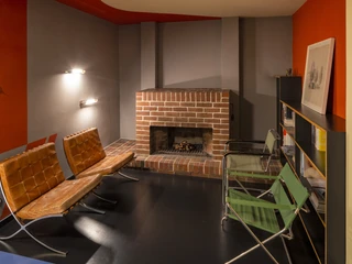 Inneneinrichtung Haus Rabe - Leipzig und Region Im Mittelpunkt steht der Kamin des Zimmers im Haus Rabe in Leipzig, welcher links und rechts von Sitzmöglichkeiten im Bauhausstil umgeben ist sowei einer Regalwand