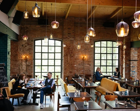 Kaiserbad - Gastronomie in Leipzig Blick in den großen Saal des Kaiserbad, mit Fokus auf den modernen Leuchten, den Backsteinwänden und den Gästen, welche ihre Mahlzeiten genießen, restaurant, kulinarik, gastronomie, freizeit