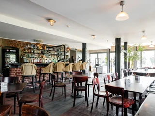 Moertelwerk - Gastronomie in Leipzig Fotografie des Innenraums des Restaurants, mit dunklem Holzmobiliar, der Bar im Hintergrund, Beleuchtung und Blick auf die großen Fenster, die helles Licht in den Saal fallen lassen, veranstaltungen, gastronomie