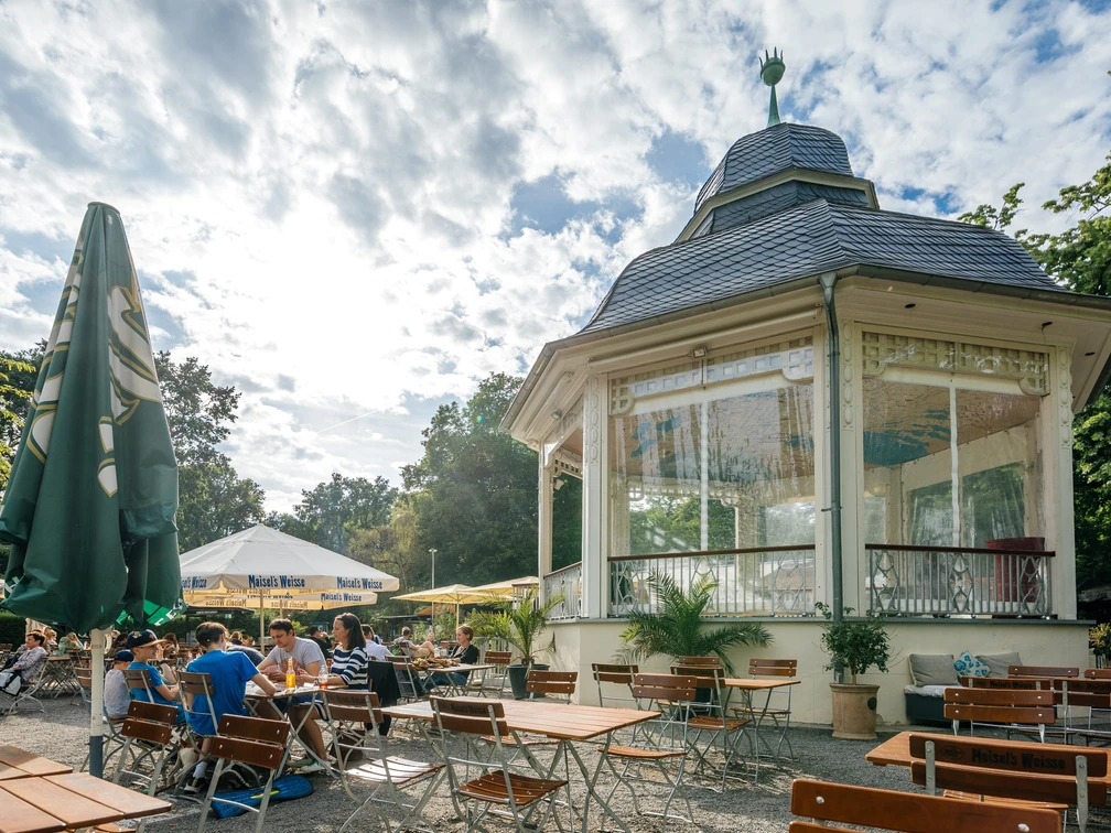 Musikpavillon - Gastronomie in Leipzig Fotografie des Freisitzes und schönen weißen Pavillons an einem Sommertag im Clara-Zetkin-Park; mit Bewaldung im Hintergrund, Sonnenschirmen