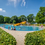 Schreberbad Leipzig - Freizeiterlebnisse in der Leipzig Region Blick auf das Hauptschwimmbecken im Schreberbad, mit gelber Rutsche und vielen Badegästen an einem Sommertag, Freizeitaktivität, Badespaß