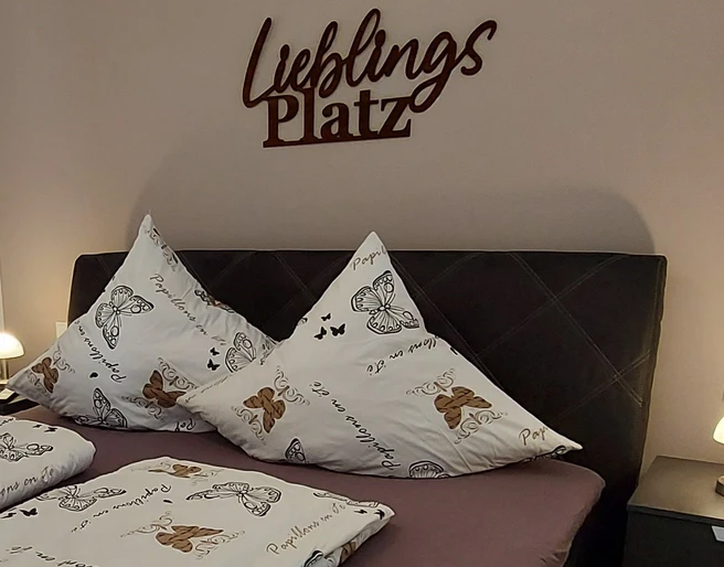 moderne_ferienwohnung_lieblingsplatz2.jpg Ein stilvoll eingerichtetes Schlafzimmer mit einem Doppelbett, dekorativen Schmetterlingskissen und sanfter Beleuchtung.