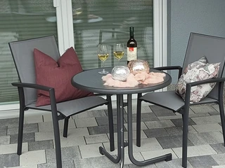 moderne_ferienwohnung_Terrasse.jpg Terrasse einer modernen Ferienwohnung mit zwei Stühlen, Tisch und Weinflasche vor einer Glastür.