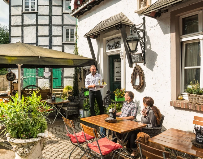 Erfrischung im Biergarten der Kutscherstuben in Wülfrath-Düssel Ein Gastro-Mitarbeiter serviert im sonnigen Biergarten zwei Gästen auf einer Terrasse Getränke.