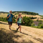 Wandergenuss in der Elfringhauser Schweiz Zwei Personen wandern auf einem grasbewachsenen Hügel mit weiten Feldern und Bäumen im Hintergrund.