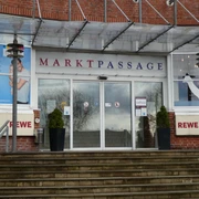 Eingang zur Markpassage mit Glastüren, flankiert von zwei Pflanzkübeln auf einer steinernen Treppe.